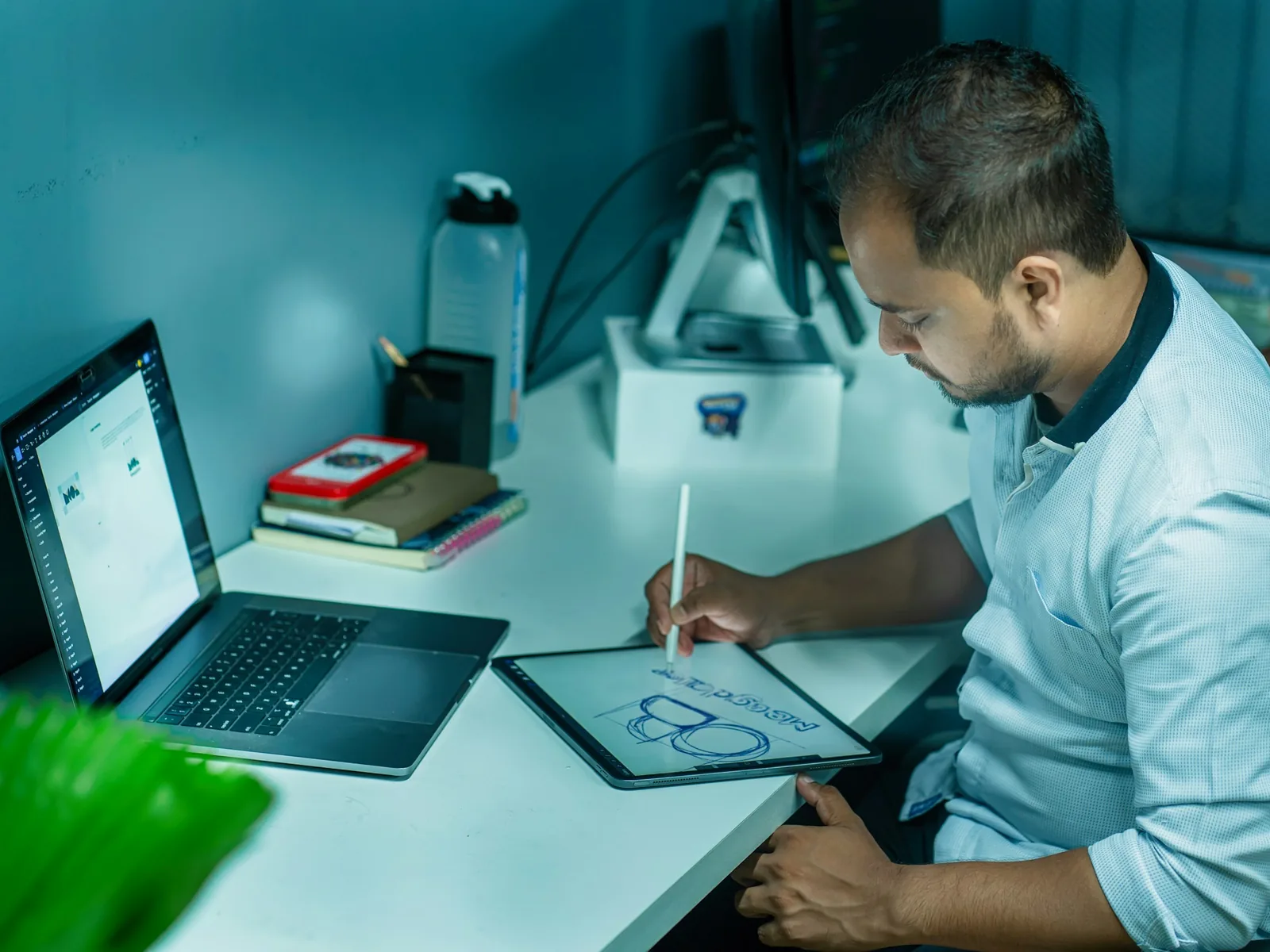 Homem a desenhar no tablet, com o portátil ao lado