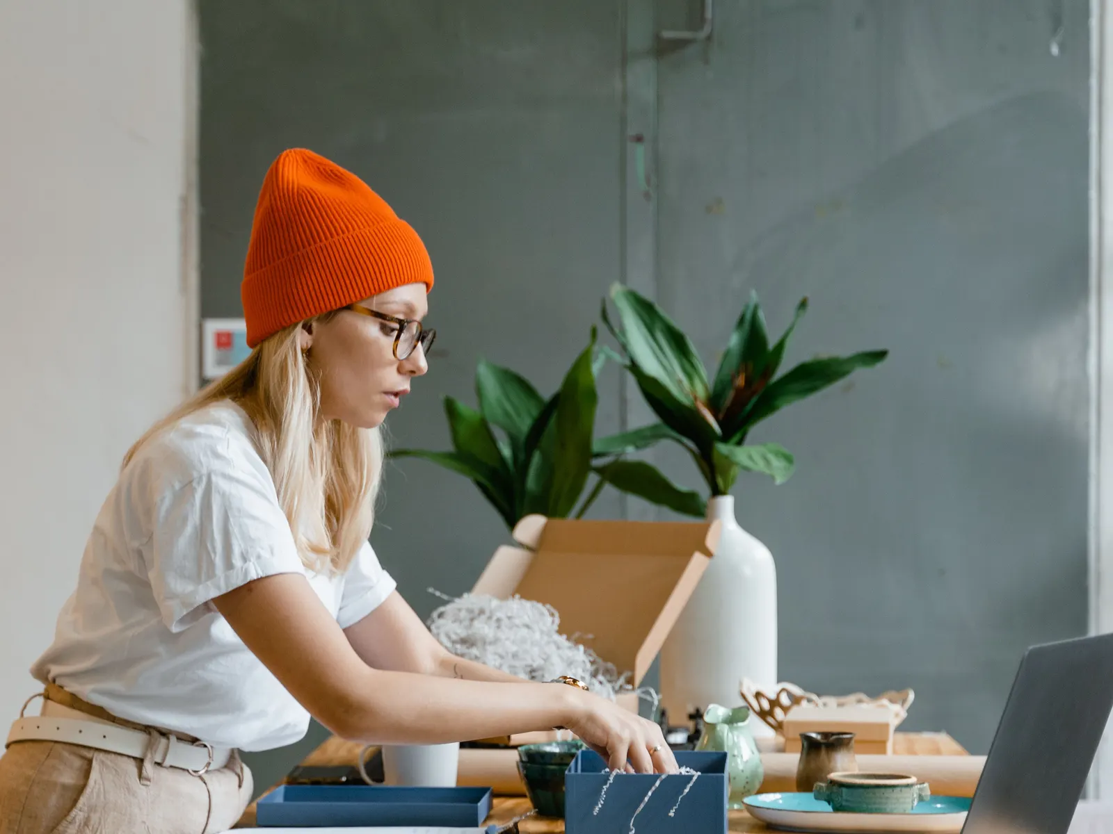 Mulher de gorro laranja a embalar produtos numa mesa com plantas