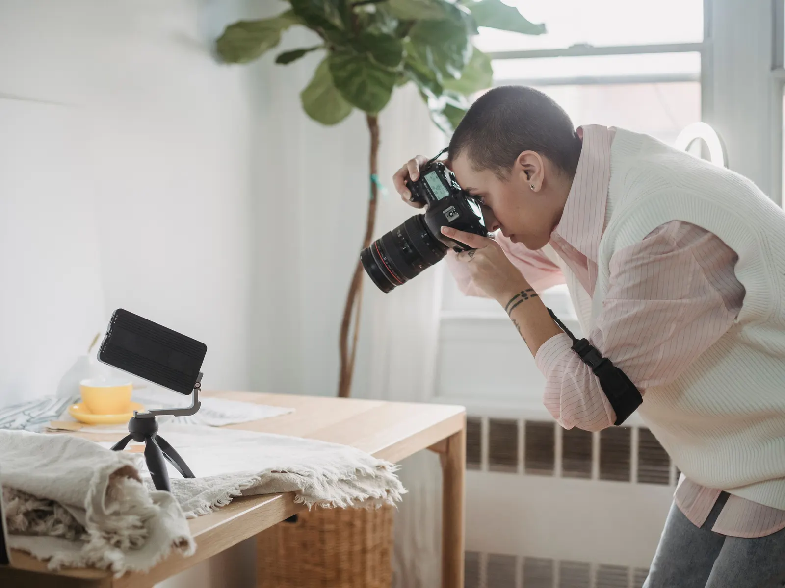 Pessoa a fotografar um produto num estúdio caseiro, com o telemóvel num tripé e luz de janela