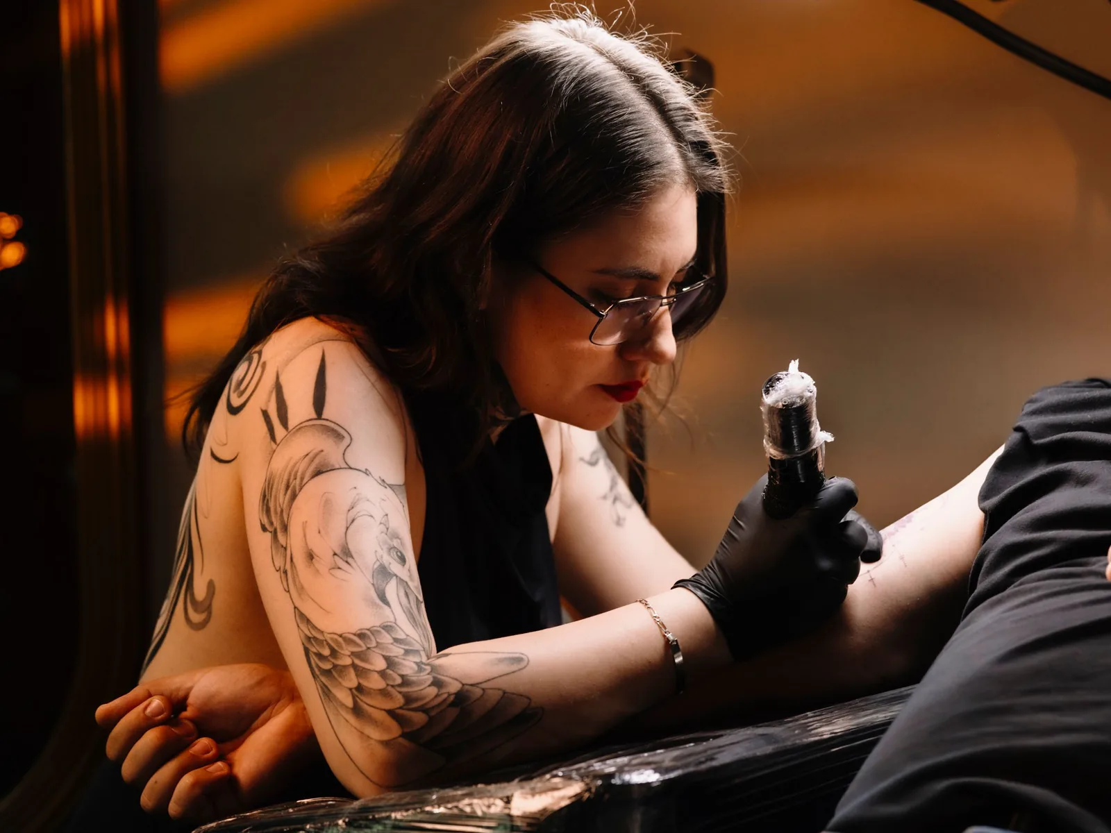 Tatuadora a trabalhar, com luz quente